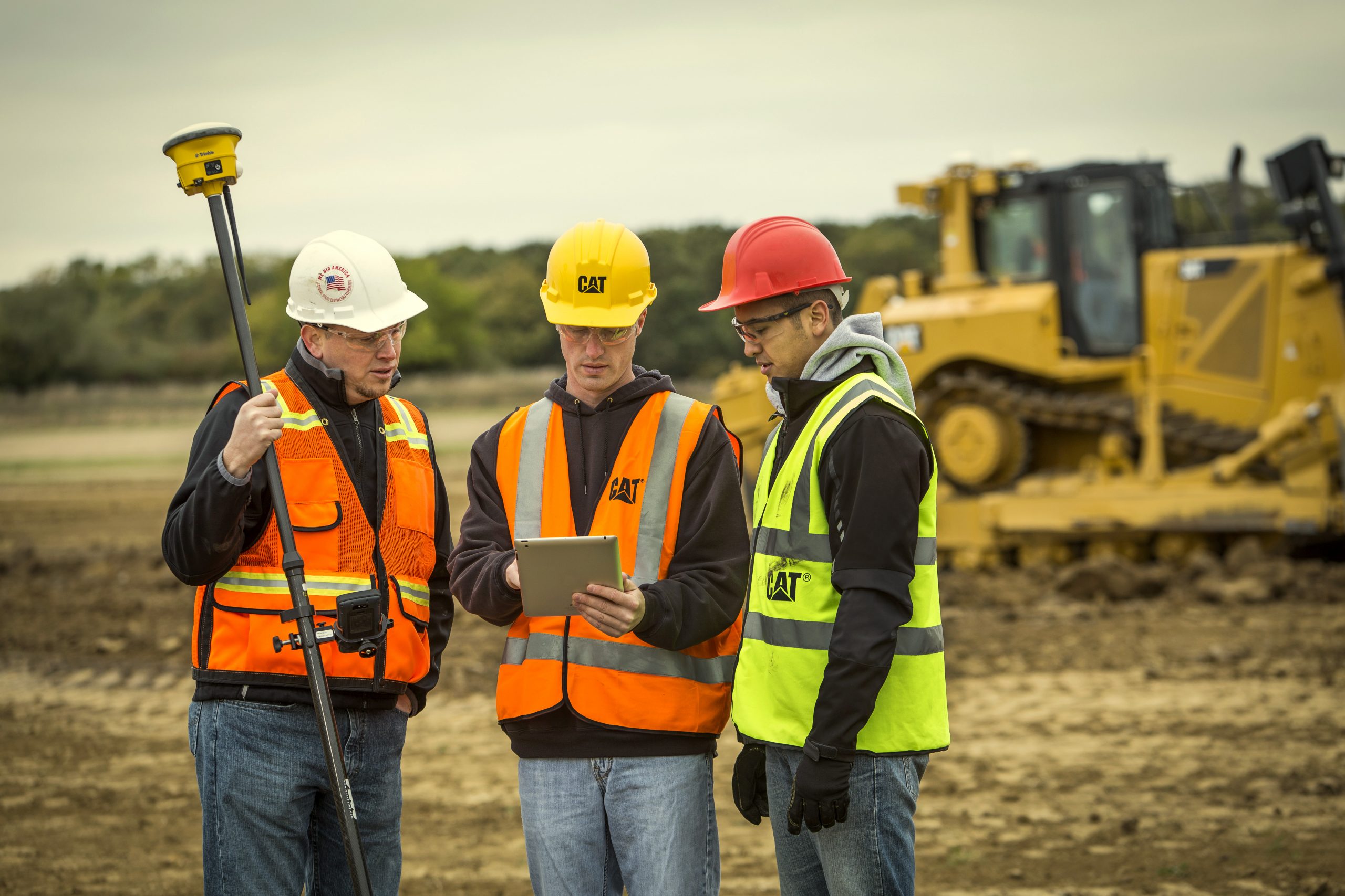 3 construction workers talking in front of heavy equipment